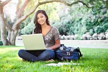 Young female adult working on a laptop while sitting in the grass under a oak tree at Addison Ranch Apartments, California, 94954